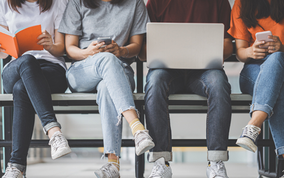 Image of 4 students with a book, 2 phones, and a laptop