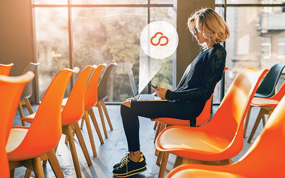 Women sitting in a chair on her laptop and phone, cloud icon coming from her laptop.